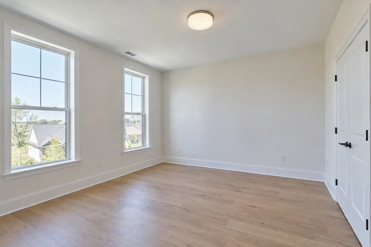 An empty bedroom with two tall windows and a pale oak floor