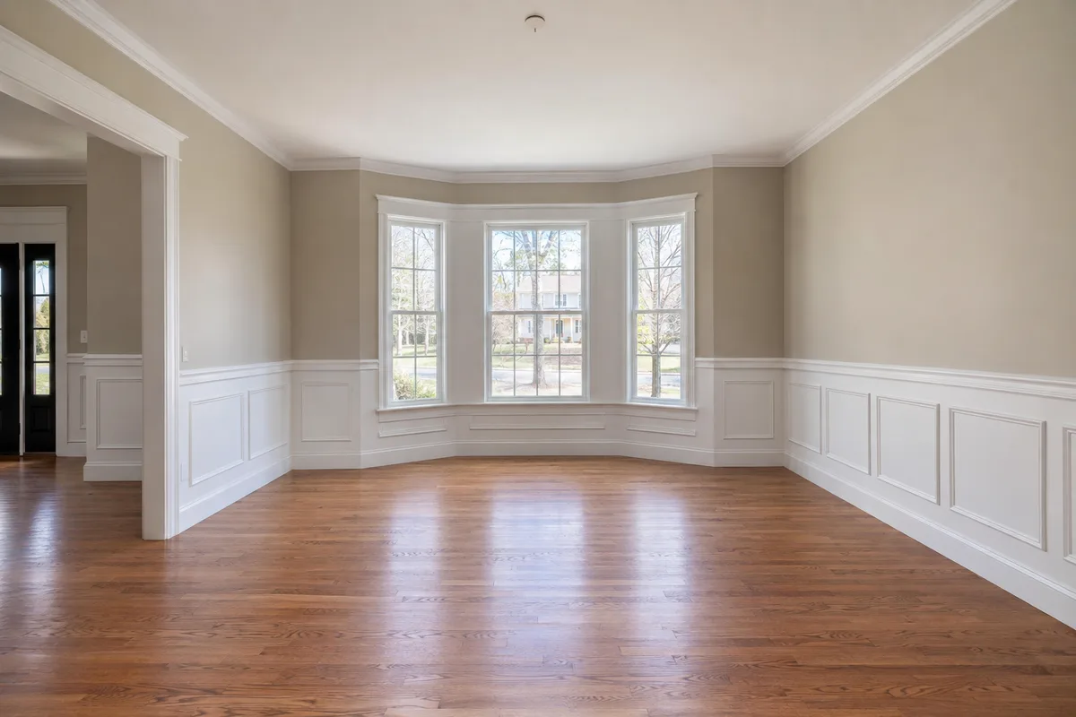 An empty dining room with wainscoting and a bay window