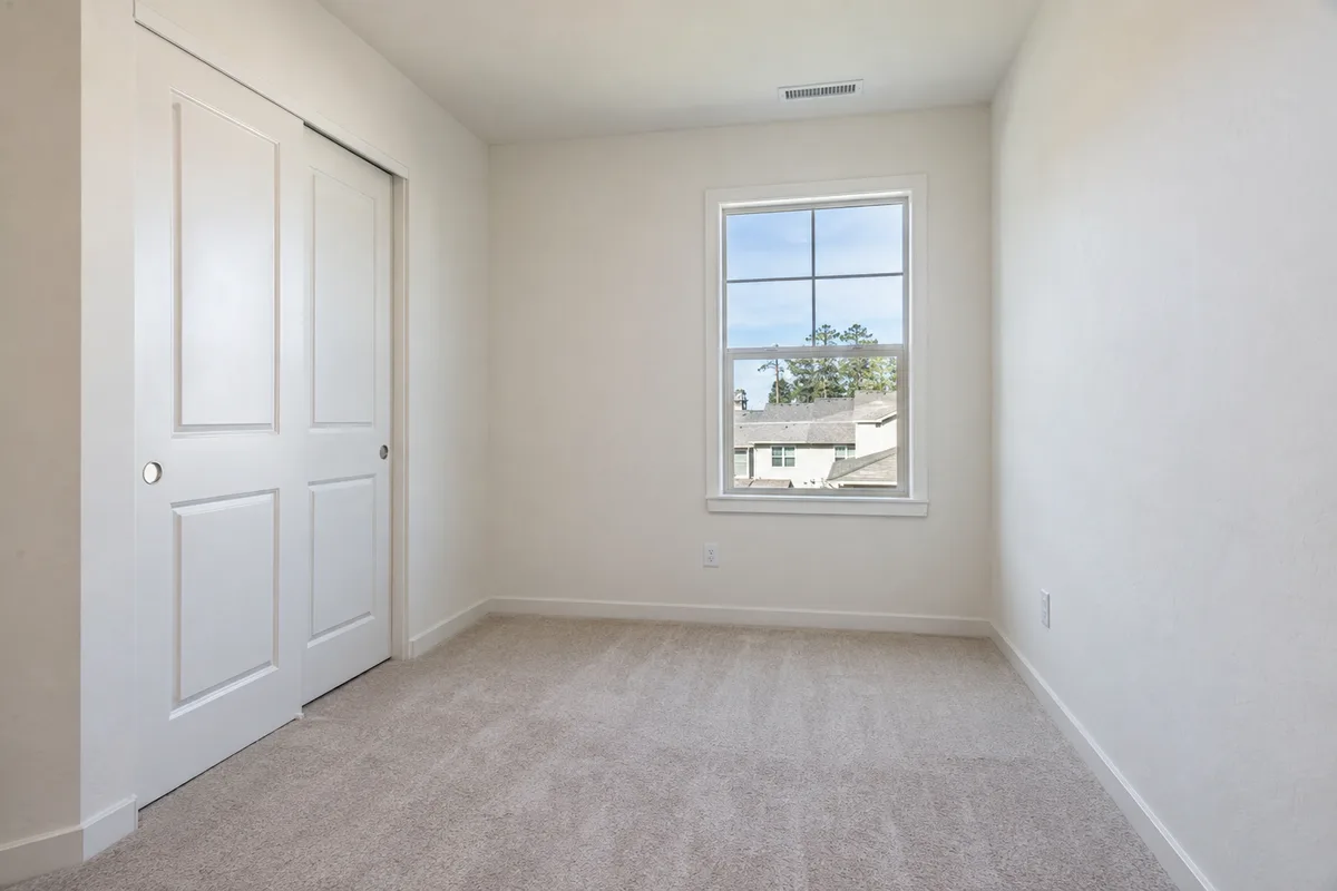A small empty bedroom with carpet and a sliding-door closet